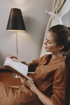 Молодая женщина с удовольствием читает книгу в кресле у торшера