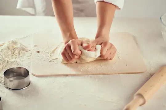 Руки повара замешивают тесто на деревянной доске