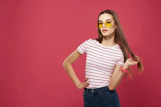 Молодая девушка в желтых очках позирует на розовом фоне