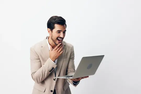 Улыбающийся мужчина в костюме работает за ноутбуком, печатая на клавиатуре