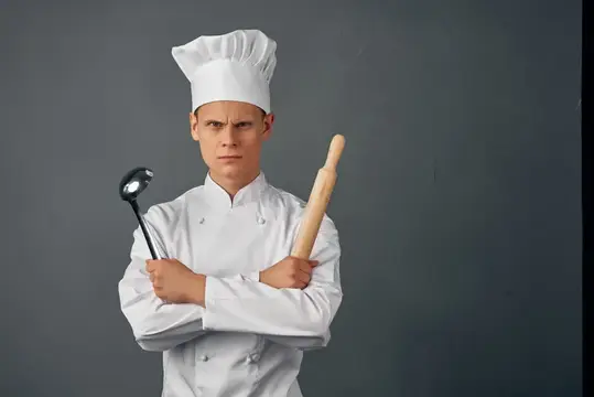 Повар в униформе с кухонными предметами, серьезный взгляд, профессионал