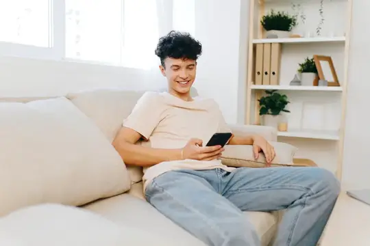 Улыбающийся кудрявый парень с телефоном отдыхает на диване