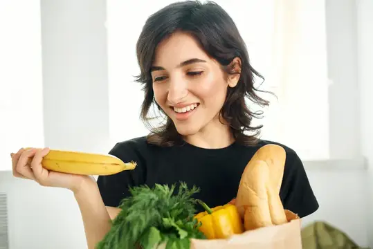 Улыбающаяся брюнетка с бананом и пакетом продуктов