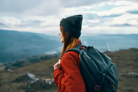 Женщина в куртке и шляпе смотрит на горы вдалеке