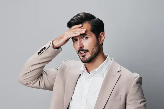 Задумчивый мужчина в бежевом пиджаке приложил руку ко лбу