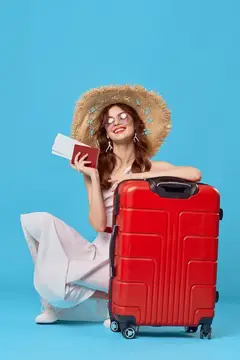 Улыбающаяся девушка в соломенной шляпе с паспортом и красным чемоданом на голубом фоне