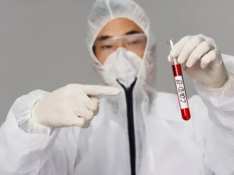 Мужчина в защитном костюме указывает на пробирку с анализом на COVID-19