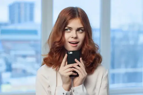 Рыжеволосая девушка с телефоном у окна в офисе