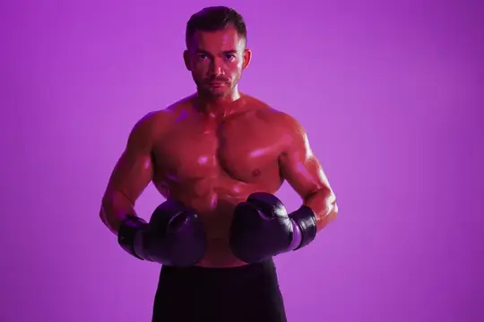 Мускулистый темноволосый боксёр с перчатками на фиолетовом фоне
