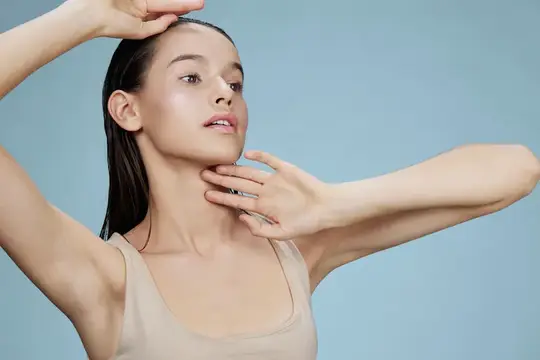 Молодая женщина с гладкой кожей касается лица на голубом фоне