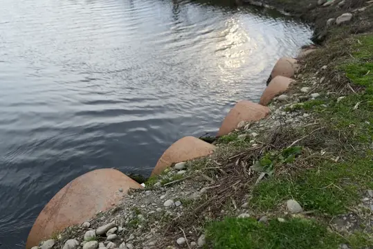 Каменные полусферы вдоль берега реки с рябью на воде