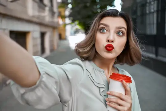 Молодая женщина с красной помадой делает селфи с кофе на улице