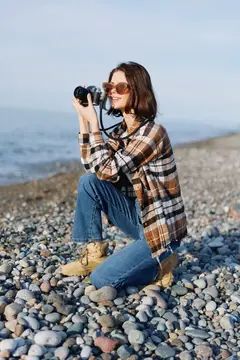 Девушка в клетчатой рубашке фотографирует на каменистом берегу
