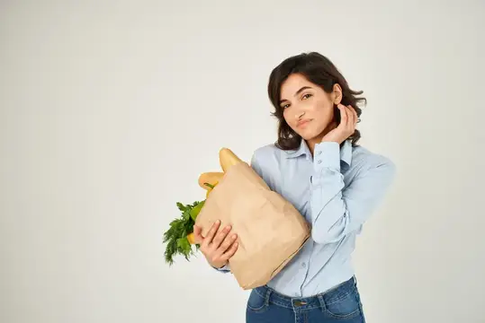Молодая женщина с бумажным пакетом продуктов на светлом фоне