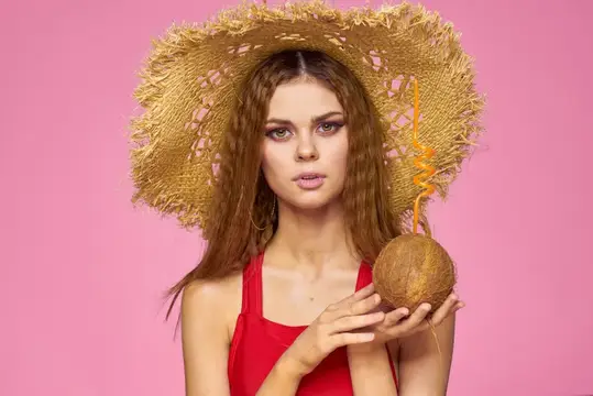 Молодая женщина в соломенной шляпе с кокосом на розовом фоне