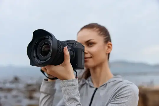 Молодая женщина с фотокамерой снимает на фоне моря и гор