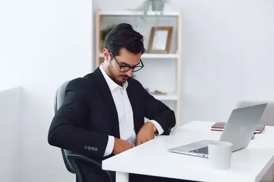 Молодой мужчина в очках и деловом костюме работает за ноутбуком в офисе