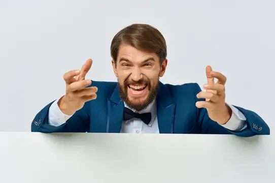 Улыбчивый бородатый мужчина в синем пиджаке и бабочке показывает пальцами