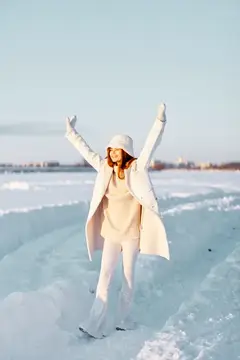 Красивая женщина в белом пальто и шапке гуляет по зимнему пейзажу, наслаждаясь свежим воздухом