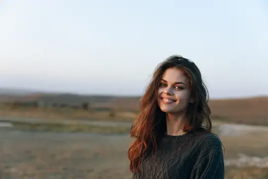 Улыбающаяся темноволосая девушка в свитере на закате в поле