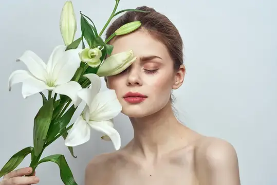 Молодая женщина с белыми лилиями у лица на сером фоне
