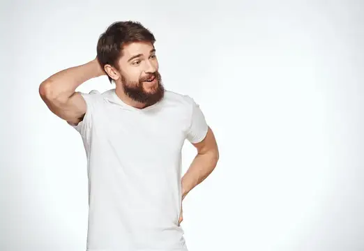 Бородатый мужчина в белой футболке задумчиво чешет затылок