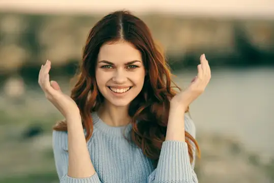 Улыбающаяся темноволосая девушка в голубом свитере на природе