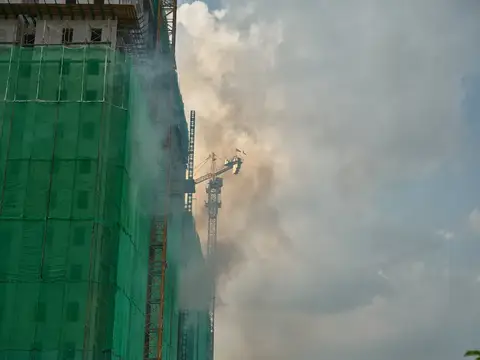 Строящееся здание в зелёной сетке и башенный кран в дыму