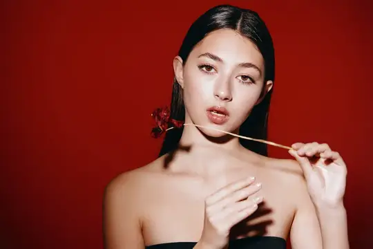 Азиатская девушка с сухоцветом у лица на красном фоне