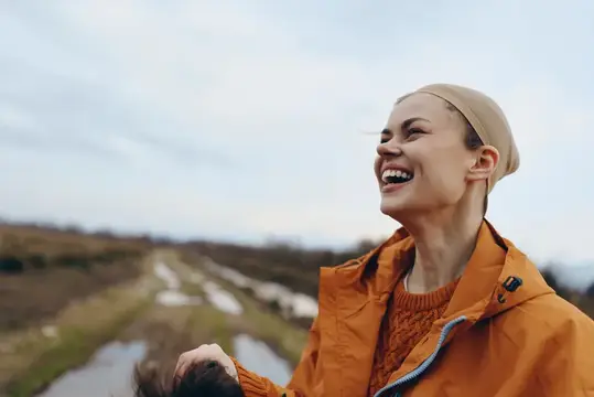 Смеющаяся девушка в оранжевой куртке на прогулке за городом