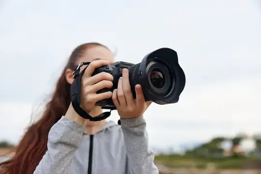 Девушка с длинными волосами фотографирует на камеру с широким объективом