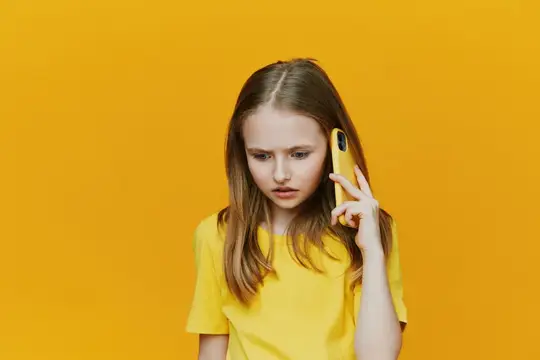 Светловолосая девочка-подросток слушает телефон на жёлтом фоне