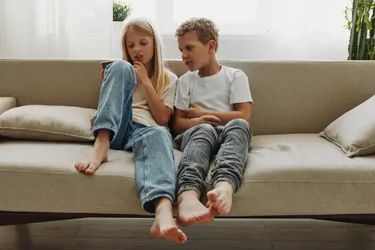 Брат и сестра сидят на диване и смотрят в смартфон