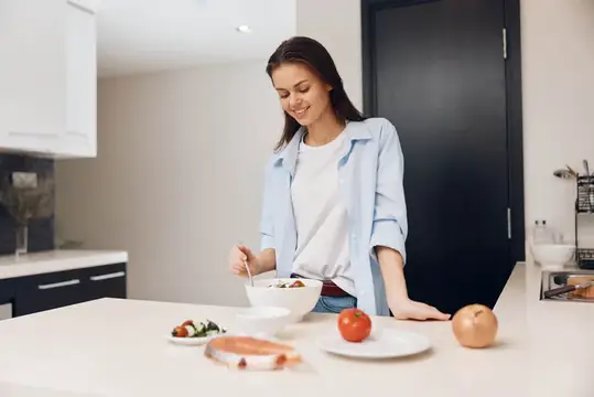 Молодая женщина готовит салат на светлой кухне