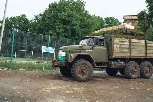 Старый армейский грузовик с деревянным кузовом стоит у забора