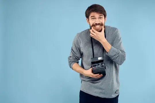 Бородатый мужчина с ретро-фотоаппаратом улыбается на голубом фоне