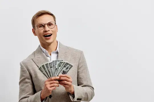 Радостный мужчина в очках и сером пиджаке держит веер из долларовых купюр