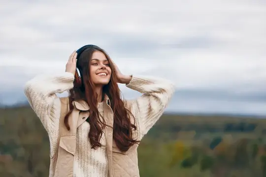 Улыбающаяся темноволосая девушка в наушниках на фоне осеннего поля