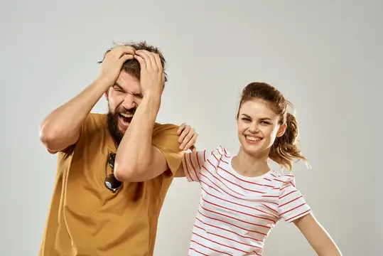 Бородатый мужчина в отчаянии хватается за голову, а улыбающаяся девушка рядом