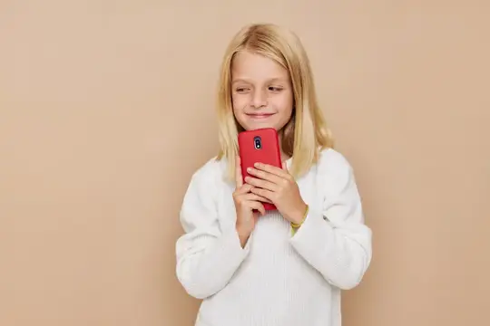 Белокурая девочка с красным смартфоном в руках на бежевом фоне
