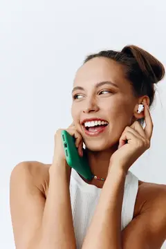 Улыбающаяся девушка с наушником держит зеленый смартфон