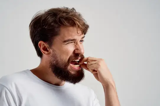 Бородатый мужчина с болью трогает зубы пальцем