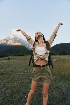 Девушка с рюкзаком раскинула руки на фоне гор