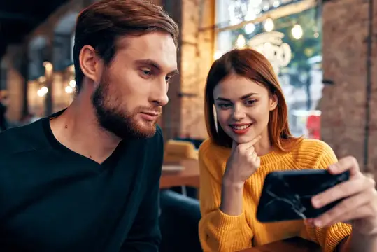 Молодая пара с интересом смотрит в смартфон в кафе