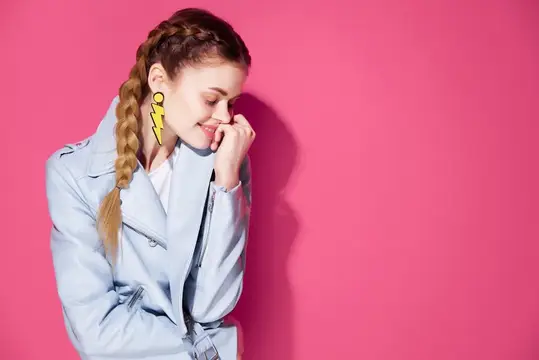 Улыбающаяся девушка с косой в голубом плаще на розовом фоне
