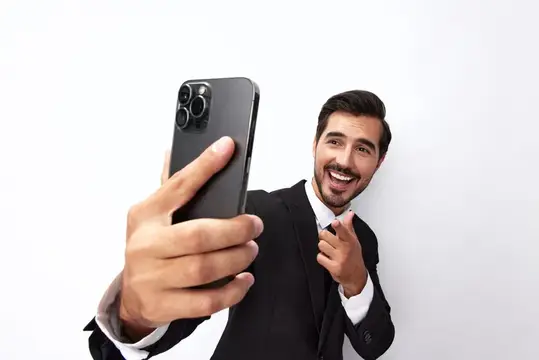 Улыбающийся бородатый мужчина в костюме делает селфи на смартфон