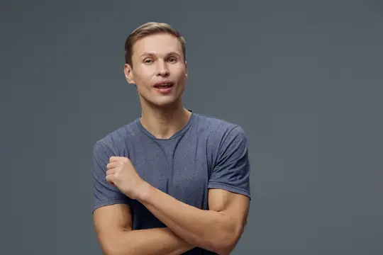 Удивлённый светловолосый парень в серой футболке на сером фоне