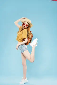 Молодая девушка в соломенной шляпе и круглых очках весело позирует на голубом фоне