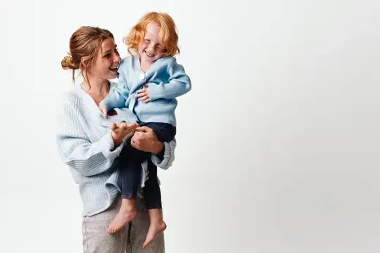 Молодая мама держит на руках смеющегося рыжеволосого малыша