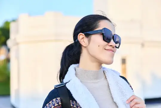 Улыбающаяся темноволосая девушка в солнцезащитных очках на улице